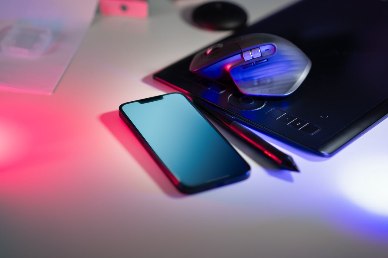 Home Modern workspace featuring a stylus tablet, smartphone, and computer mouse under colorful lighting.